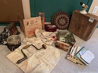 Full lot overview showing toaster, hot plate, wooden box, hand drill, mats, cloth bags, tins, and booklets