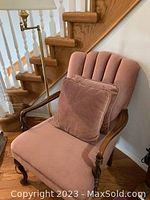 Dusty pink upholstered chair with matching cushion positioned at stairway corner with wooden arms and carved legs visible