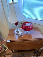 Ruby red punch bowl, silver candy dish, and a lamp on a wooden table.