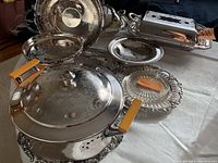 Wide view of multiple silver plated serving dishes including covered dish, tray, rectangular dish with lid, and plates on table.