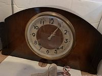 Wooden mantel clock with round dial, key in front, pendulum window below dial.