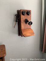 Wooden wall telephone mounted on wall showing front with two black bells and hanging handset.