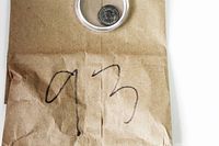 Photo of ancient coin encased in clear protective holder placed on a brown paper bag with '93' written on it.