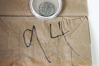 Ancient Roman coin in a clear protective capsule placed on brown paper with markings underneath.