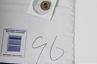 Photo showing an ancient coin in a white protective holder with handwritten '96' and a barcode on the packaging.