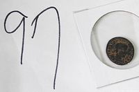 Photo of a rare ancient coin in a protective holder next to a handwritten number 97.