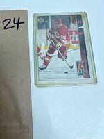 Hockey trading card showing a player in red and yellow uniform with number 26 in action on the ice, with visible wear and minor damage.