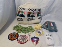 Photo of the full lot including the white knit hat with Olympics design, patches, pins, and two medal cases.