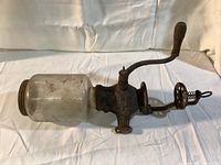 Full side view of coffee grinder showing glass hopper, cast iron body with embossed details, handle and crank arm extended horizontally.