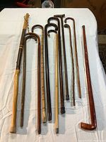 Eleven wooden canes and walking stick laid out on white cloth showing shapes, handles, and finishes