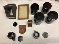 Overall view of four Canon lens cases, two Auto-Topcor lenses, small leather pouches, plastic hood, lens caps, and wooden frame.