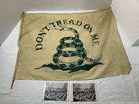 Overall view of Don't Tread On Me cloth banner laid flat with two Concord bicentennial postcards placed below.