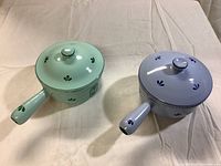 Top view of green and blue enamel Dru saucepans with lids, showing tulip pattern and handles.