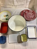 Overview of the 9 enamelware items including the red speckled plates, white stew pot, decorative bowl, and various trays and small containers.