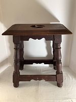 Front view of wooden stool showing turned legs and stretcher supports, dark stained wood with slight wear.