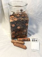 Front view of the glass jar half-filled with pennies and three penny rolls placed in front