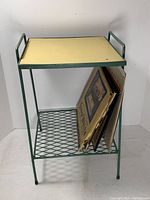 Front angle view of green metal LP table with yellow top and metal mesh bottom shelf holding vintage record albums.