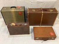Four vintage luggage pieces with varying colors and sizes arranged on a white cloth background showing exterior details and size comparison.