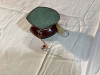 Angled side view of the Tibetan hand drum showing green drumhead, polished reddish-brown wooden frame, and attached string with wooden bead.