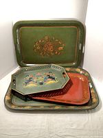 Four vintage hand-painted metal serving trays stacked and displayed showing various sizes, colors, and floral designs.