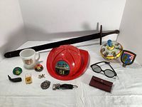 Full overview of lot showing sword, fire helmet, mug, tops, ring, glasses, wallet, badges and other small toys.