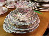 Stacked teacup on two saucers, four salad plates, two lunch plates, one serving plate with floral design and gold trim