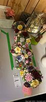 Nine assorted porcelain china floral arrangements placed on white surface with wood background, varying flower colors and sizes.