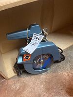 Black and Decker corded circular saw placed on a wooden shelf showing the 7-inch blade and power cord.