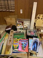 Overview of assorted craft supplies including colored pencils, brush sets, vintage wooden model ship parts, and various stored items in plastic containers and boxes.