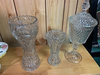 Photo showing two crystal vases and one lidded crystal compote on wooden surface against wood panel background