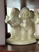 Front view of two snowbabies holding candles on oval base in faux wood display cabinet.