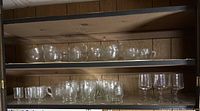 Two wooden shelves with multiple clear glass cups and glasses arranged side by side.