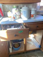 Full view of ceramic jars, mugs, and kitchen storage on countertop and inside cabinet below.