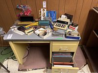Overview of various office accessories on a yellow desk in a basement setting, showing general condition and item variety.