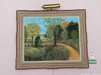 Framed landscape painting on wall showing full frame and mounted gallery light