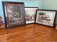 Three framed artworks displayed on a wooden floor, two prints and one photo.