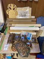 Photo showing assorted rolled posters, cardboard sleeves, lion crest, and metal owl wall art arranged on a table.
