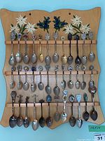 Full view of wooden wall mounted rack with 39 collector spoons arranged on it.