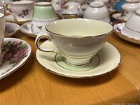 Photo showing cream colored teacup and saucer with gold trim, marked H&M on bottom indicating fine bone china made in England.
