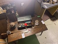 Photo showing entire lot on wooden table - fishing rod with spinning reel, open metal tackle box with lures and fishing lines, and vintage lantern