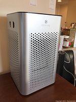 Front angle photo showcasing the perforated metal panel design and Medify Air logo on top front of the device.