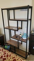 Front view of bookcase showing five wood-look formica shelves with black metal frame and some items on shelves for scale.