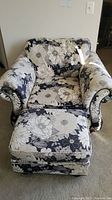 Blue, off white and tan floral patterned armchair with matching ottoman visible from an angled front view.