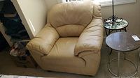 Front view of tan leather-like armchair showing cushioned seat, backrest, and armrests, with some visible staining.