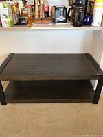 Full front view of the coffee table showing the dark wood top and lower shelf with black metal legs and trim.