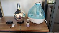 Electric diffuser, humidifier, lavender oil bottle and power adapter placed on a wooden table against a white wall.