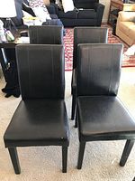 Front view of four matching black padded dining chairs arranged in two rows.