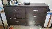 Front view showing the six drawers and silver curved handles on the dark brown dresser with some personal items on top.