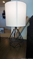 Front view of one lamp showing geometric metal base and white fabric shade on dark wooden table.