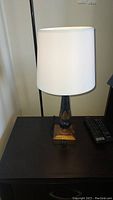Table lamp with white lampshade, dark wood and black base on a dark table